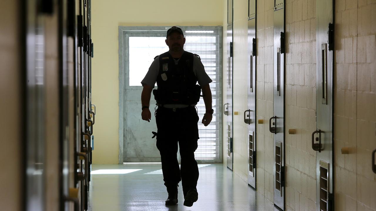 A corrections officer walks down a cell corridor.
