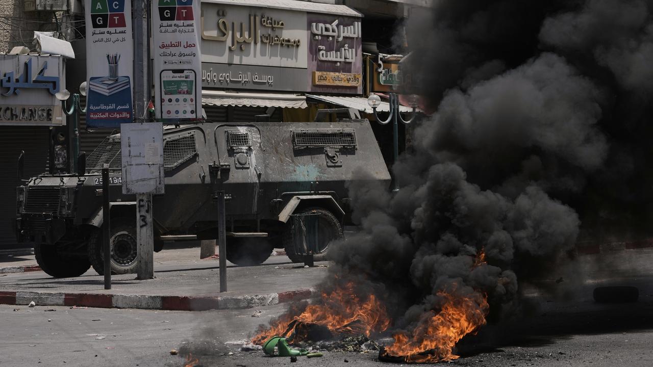 An armoured vehicle drives near burning tires in Nablus.