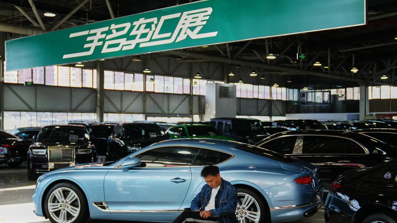 A man sits near luxury cars at a second hand market in Beijing