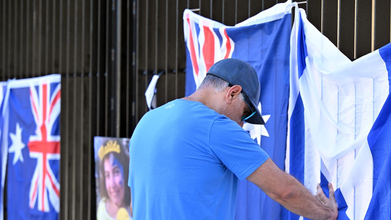 A man puts his hand on the Israeli flag at a makeshift memorial
