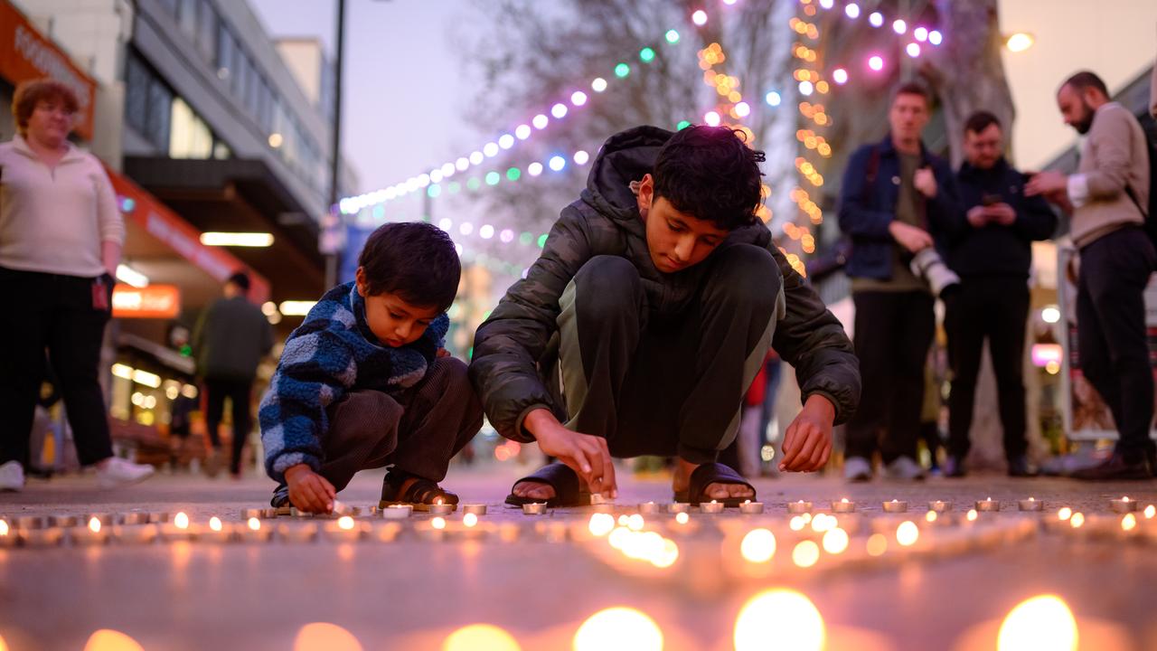 Children place candles on the floor during a candle vigil