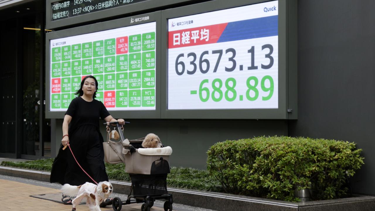 A woman walks past a stock market indicator board in Tokyo